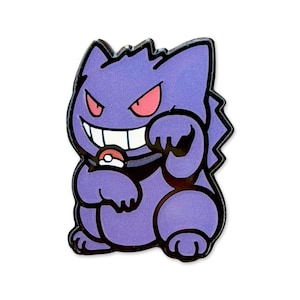 Può includere: Una spilla smaltata viola raffigurante il personaggio Gengar della serie Pokémon. La spilla ha un contorno nero, occhi rossi e un sorriso con denti bianchi. Tiene una Poké Ball.