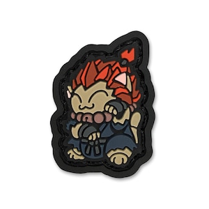 May include: A colorful patch featuring a cartoon character with red hair, a tan face, and a blue outfit. The patch has a black border and is likely made of rubber or a similar material. The character is smiling and appears to be in a fighting stance.