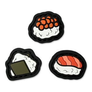 May include: Three sushi-themed charms with black borders. One charm features orange roe, another has a nori seaweed wrap, and the third displays salmon. All are set against a white background.