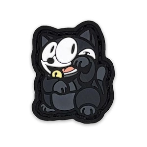 Puede incluir: Parche de gato de dibujos animados en blanco y negro, con una cara sonriente, ojos grandes y un objeto amarillo en la boca. El parche tiene un borde negro y está sobre un fondo blanco.