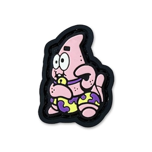 May include: A pink Patrick Star character charm with a black outline. The character has wide eyes, a purple collar with a yellow bell, and wears yellow and purple patterned shorts. The design is rendered in a flat, cartoon style with bold lines.