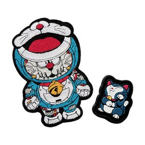 May include: Two embroidered patches featuring a robot cat character with a bell and a smaller cat character with a bell. The robot cat is wearing a blue and white suit with a red and white hat. The smaller cat is blue and white with a red collar.
