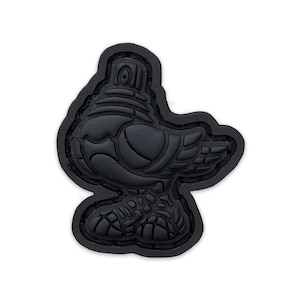 May include: Black rubber patch shaped like a bird with a detailed design. The bird has a large head with a round, raised detail on top. The bird's body is detailed with a textured pattern.