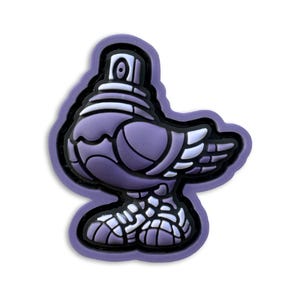 May include: A purple and white shoe charm shaped like a pigeon with a spray paint nozzle for a head. The design features a stylized bird body with layered wing details and textured feet, outlined in a thick purple border on a black base.