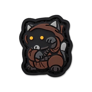 May include: A black, brown, and gray patch featuring a cartoon-style creature with yellow eyes, wearing a hooded outfit. The patch has a black border and a unique design, suitable for collectors or fans of pop culture.