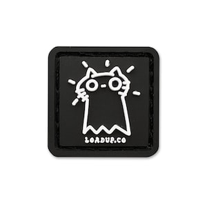 May include: A square black patch with rounded corners featuring a white line art graphic of a cat-like figure with large circular eyes and radiating lines. The text LOADUP.CO is printed in white at the bottom of the patch.