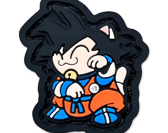May include: A black, die-cut patch featuring a cartoon character with black hair, cat ears, and an orange and blue outfit. The character is smiling and has a gold bell around its neck. The patch has the Japanese character "悟" on the chest.