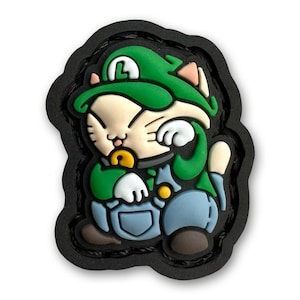 May include: A green and blue cartoon cat wearing a green hat with an 'L' on it. The cat is sitting with its head in its hands and has a pacifier in its mouth.