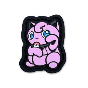 May include: A pink, rounded character patch with large blue eyes, pointed ears, and a small tuft of hair on top. The character is holding a small, round, red and white ball near its mouth, outlined in a thick black border against a white background.