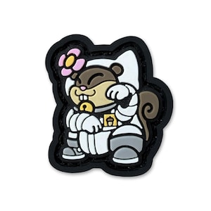 Può includere: Un ciondolo in gomma raffigurante uno scoiattolo marrone che indossa una tuta spaziale bianca, con un fiore rosa sulla testa, un collare con campanellino giallo e una piccola toppa quadrata gialla con icona di ghianda sul petto, bordato di nero.