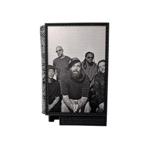 May include: Black and white photo of a band with five members. The photo is framed in a black frame with a silver background. The frame has the text "Elysium Threads" on the bottom.