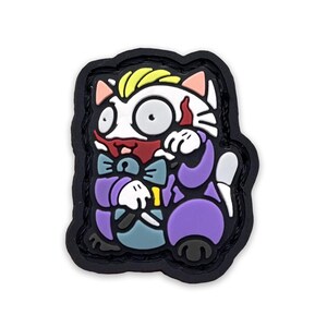 Puede incluir: Un parche colorido con un personaje de gato de dibujos animados con una cara blanca, pelo amarillo y un traje morado. El gato tiene una boca roja y una pajarita azul. El parche tiene un borde negro.