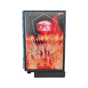 Puede incluir: Una imagen enmarcada en negro de una banda tocando en un escenario con una gran forma geométrica roja colgando sobre ellos. La imagen está enmarcada con un borde negro y las palabras "Elysium Threads" están impresas en la parte inferior del marco.