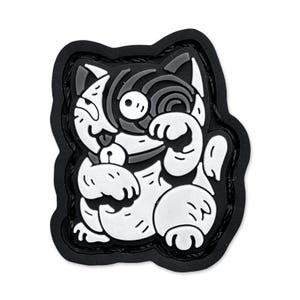 May include: A black, white, and gray cat-shaped patch with a unique design. The cat is depicted in a cartoon style, with one paw raised. The patch has a black border and is likely made of rubber or a similar material.