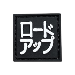 Puede incluir: Un parche cuadrado negro con caracteres japoneses blancos. El texto dice "ロードアップ" en una fuente sans-serif en negrita. El parche tiene un borde texturizado y está sobre un fondo blanco.