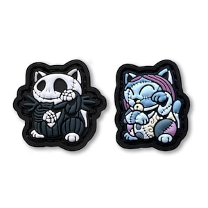 May include: Two black and white cat-shaped patches with a stitched design. One patch features a black and white cat with a stitched face and a black and white striped body. The other patch features a blue and white cat with a stitched face and a blue and white striped body.