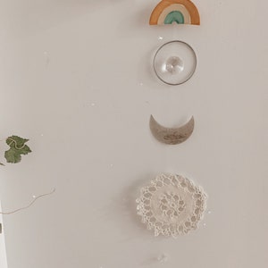 Puede incluir: Una pared blanca con un arcoíris, un atrapasol de cristal, una luna creciente, un encaje blanco de ganchillo y un cristal colgando del techo.