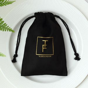 Può includere: Borsa a cordoncino in velluto nero con logo dorato che dice "Tailored of Faith Co."