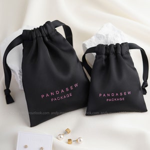Puede incluir: Dos bolsas de cordón negro con texto blanco que dice "Pandasew Package".