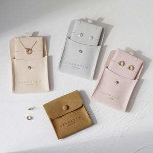 May include: An assortment of jewelry pouches in beige, gray, and pink, each containing jewelry. The pouches are made of a soft material and have a snap closure. The text "PANDASEW PACKAGE" is printed on each pouch.
