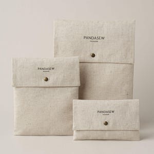 May include: Three rectangular beige fabric pouches of varying sizes, each featuring a flap closure secured with a single brass-colored metal snap button. The text PANDASEW PACKAGE is printed in black ink on the front of each pouch.