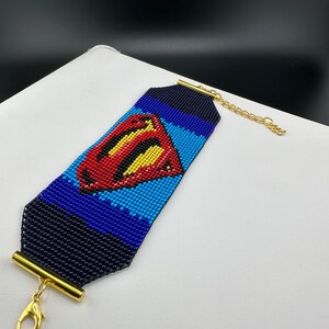 May include: A beaded bracelet with a Superman logo in red, yellow, and blue colors. The bracelet has a gold clasp and a gold toggle closure.