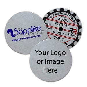 May include: Three silver metal round stickers. The first sticker has a blue logo with the text "The Sapphire Squirrel" and the website "thesapphiresquirrel.etsy.com". The second sticker has black text on a silver background with the text "Your Logo or Image Here". The third sticker has black text on a silver background with the text "REEVES RACING GARAGE", "MODEL A 555", "4770747", "ASSY NO LD DATE 5 28 11 GARAGE 350 1 Y."
