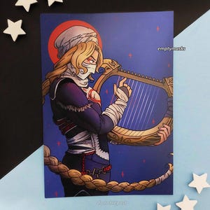 May include: A rectangular art print featuring a blonde character with a white head covering and face mask, wearing a dark blue outfit with red accents, playing a golden harp. The background is a deep blue with a red circle and small red crosses.