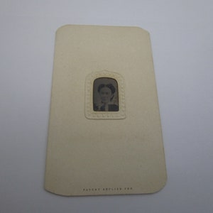 May include: A vintage photo card with a small oval-shaped window featuring a black and white portrait of a person. The card is cream colored and has the text "Patent Applied For" printed at the bottom.