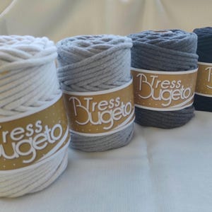 May include: Four spools of thick cotton rope yarn in white, gray, light gray, and black. Each spool has a gold label with the text "Tress Bugeto".