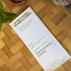 May include: A rectangular notepad titled project notes, thoughts & tallies with floral borders. The paper features sections for notes, thoughts, and tally marks, with handwritten entries including numbers like 38 and 20, and a bottom line for pattern.