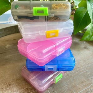 May include: Stack of four clear plastic storage containers with colorful latches. The containers are stacked in order from largest to smallest. The top container is gray, the second is clear, the third is pink, and the bottom is blue.