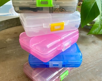 May include: Stack of four clear plastic storage containers with colorful latches. The containers are stacked in order from largest to smallest. The top container is gray, the second is clear, the third is pink, and the bottom is blue.