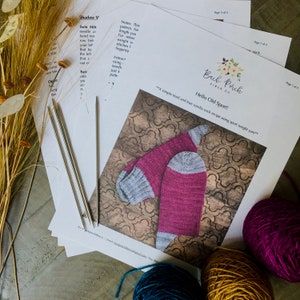 May include: A knitting pattern for a pair of socks called "Hello Old Sport!" by Back Porch Fiber Co. The pattern includes instructions for using sport weight yarn and a photo of the finished socks.