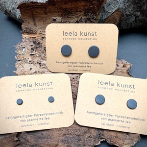 May include: Three cards with the text "leela kunst SCHMUCK KOLLEKTION" and the text "handgefertigter Porzellanschmuck von jeannette lee versilbert - nickelfrei". Each card has two black porcelain earrings.