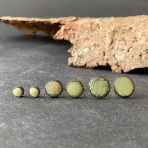 Op de afbeelding: Een set van zes ronde keramische oorbellen in verschillende maten. De oorbellen zijn groen en geel met een gespikkelde textuur.