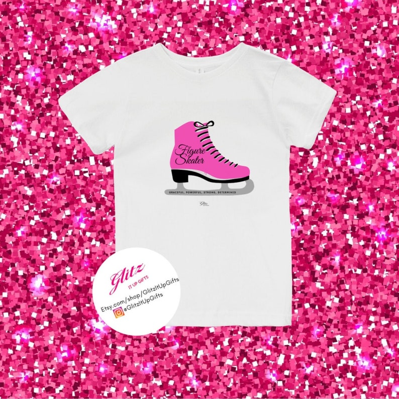 May include: White t-shirt with a pink figure skate graphic and the text "Figure Skater". The text below the skate reads "Graceful, Powerful, Strong, Determined".