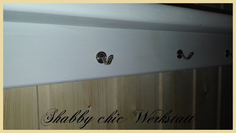 May include: White wooden shelf with three silver hooks. The shelf has a wood grain pattern and the text "Shabby chic Werkstatt" is written below the shelf.