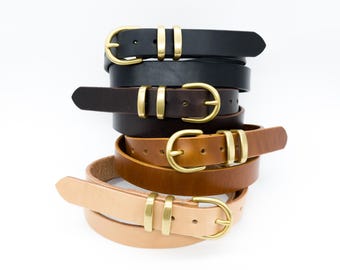 May include: A stack of five leather belts in various shades of brown and black. Each belt features a gold-colored buckle and a matching gold-colored loop. The belts are stacked on top of each other against a white background.