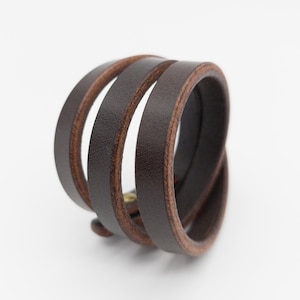 May include: A dark brown leather wrap bracelet with three bands. The bracelet is wrapped around itself, creating a layered effect. The edges of the leather are a lighter brown. The bracelet is on a white background.