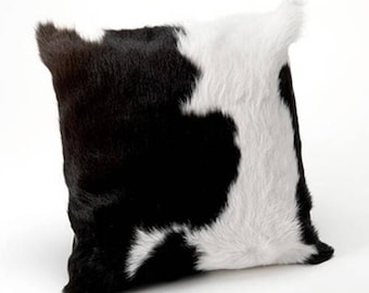 May include: Black and white cowhide cushion with a soft, fuzzy texture. The cushion is rectangular and has a unique, natural pattern.