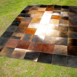 Könnte beinhalten: Ein Patchwork-Rinderfellteppich mit Quadraten aus braunem, schwarzem und weißem Leder. Der Teppich besteht aus verschiedenen Teilen von Rinderfell, die zusammengenäht wurden, um ein einzigartiges Design zu schaffen.