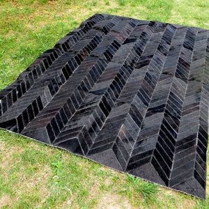 May include: Black and white cowhide rug with a herringbone pattern. The rug is made of leather and has a natural, rustic look.