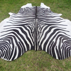 May include: Black and white zebra hide rug with a natural, organic shape. The rug has a symmetrical pattern of stripes.