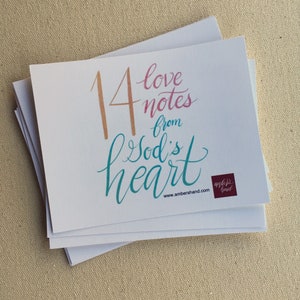 May include: A stack of white square cards with the text "14 love notes from God's heart" in a script font. The numbers and text are in shades of peach, pink, and teal. The cards have the ambershand.com logo.