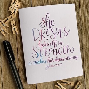 May include: A watercolour-style card with the text "She dresses herself in strength & makes her arms strong Prov. 31:17" in a purple, pink and blue gradient.