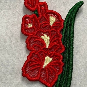 May include: Red and white embroidered flower with green leaves. The flower is a delicate lace design.