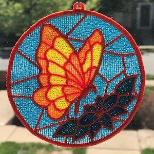 May include: A round, red-trimmed, embroidered window hanging with a blue background. A yellow and orange butterfly is centered on the hanging with a dark green flower below it.