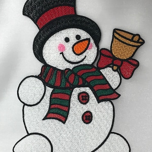 May include: A white snowman with a black top hat, red and green striped scarf, and a gold bell in its right hand. The snowman has a carrot nose, black eyes, and pink cheeks.