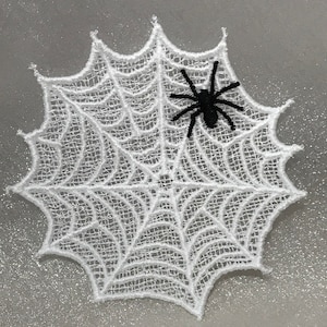May include: White lace spiderweb with a black spider in the center. The spiderweb is a decorative item for Halloween.